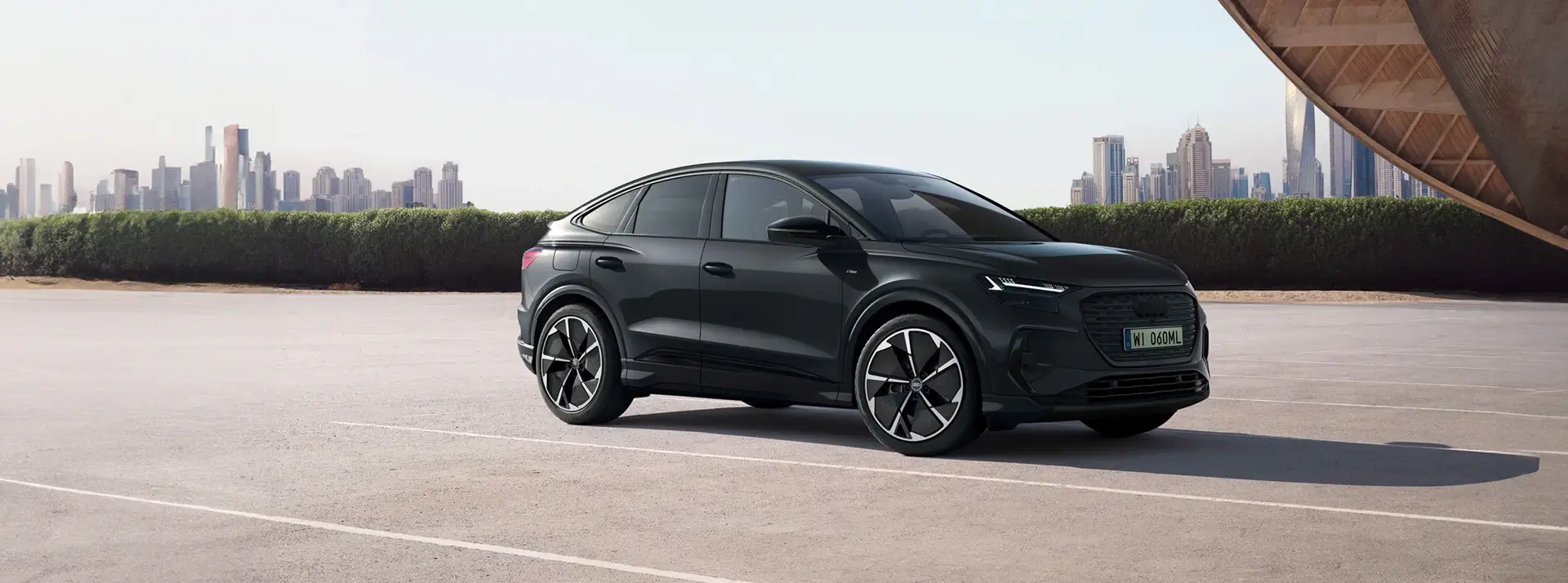 betonowy parking, w oddali wieżowce, na parkingu stoi duży czarny SUV Audi Q6 Sportback e-tron