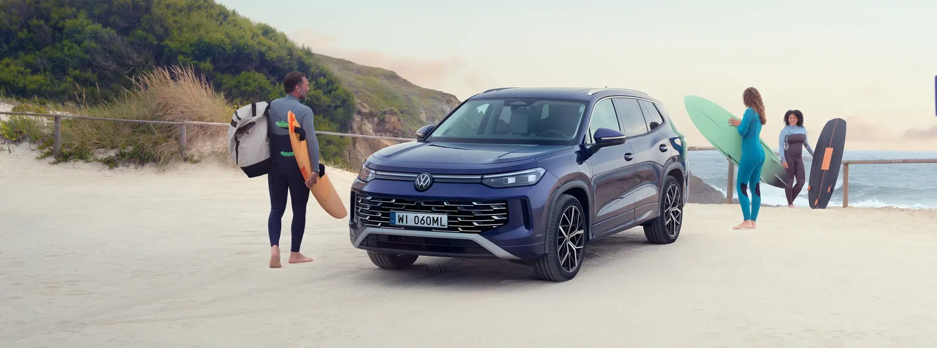 surferzy na plaży obok dużego SUV-a Volkswagen Tayron w kolorze granatowym